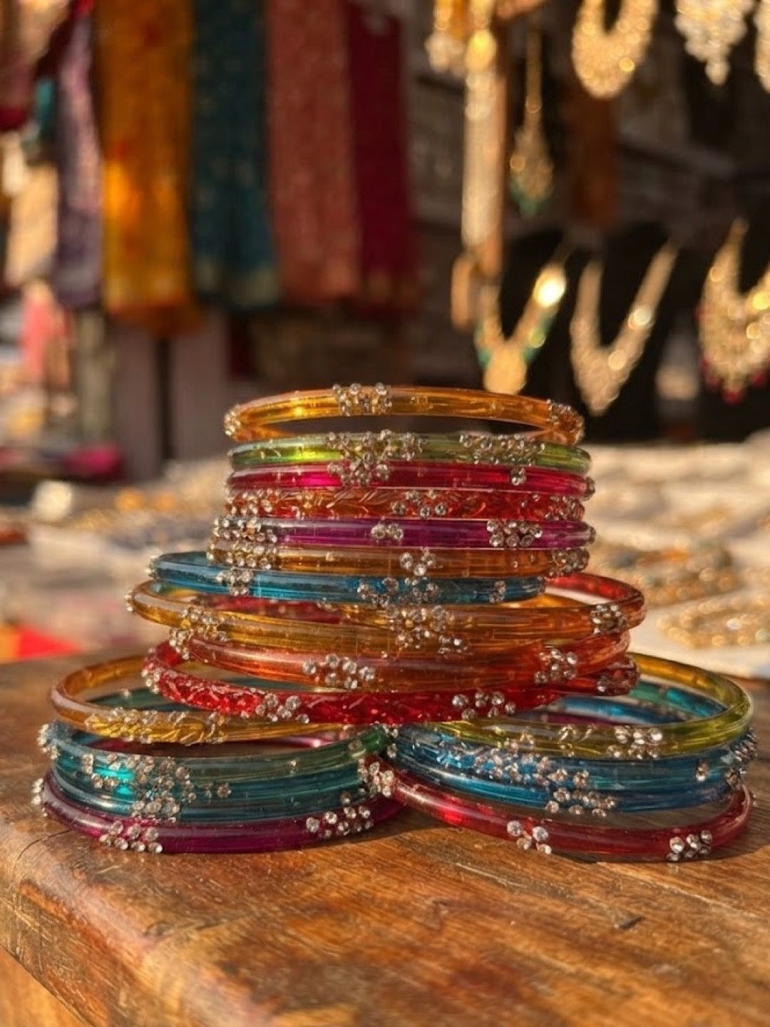 A stack of rainbow glass chudiyan with sparkling stone flowers, on a wooden table