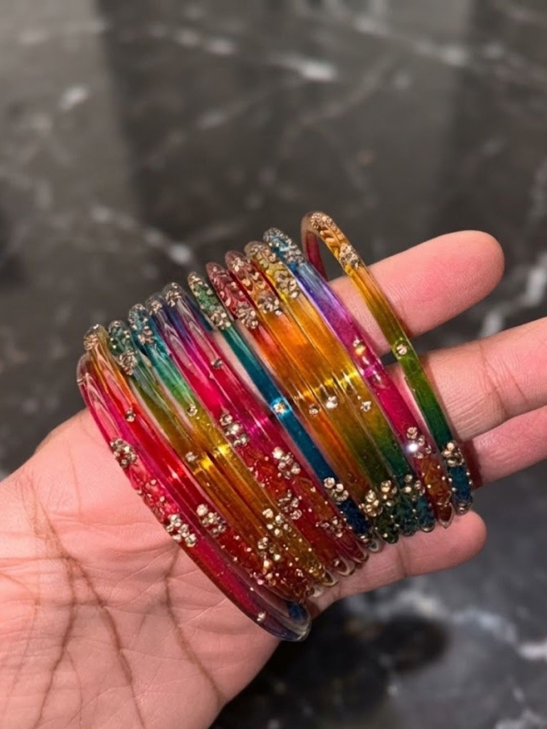 The chudiyan held in a hand, each one blending from pink to yellow to green and blue
